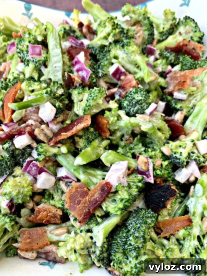 Keto Low-Carb Broccoli Salad with Bacon being mixed in a bowl, showing fresh broccoli, red onions, sunflower seeds, and crispy bacon
