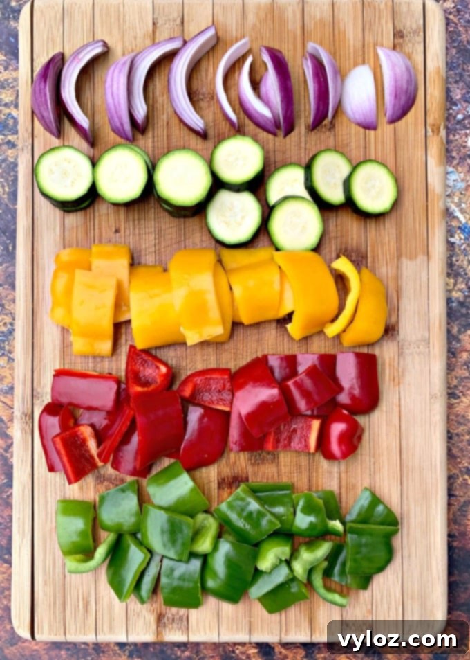 Freshly cut bell peppers, zucchini, and red onions on a cutting board, ready for air fryer chicken kebabs.