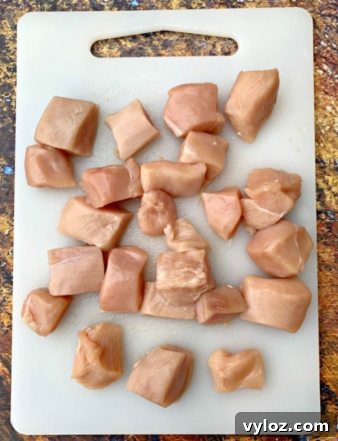 Raw chicken breast cut into uniform 1-inch cubes on a cutting board, ready for marination.