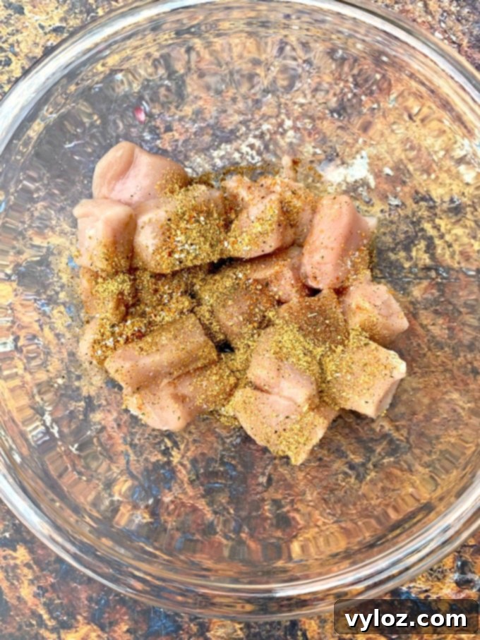 Raw chicken cubes marinating in a glass bowl with a rich seasoning blend.