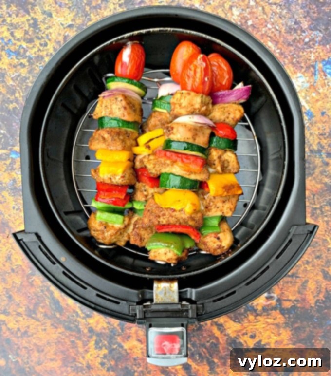 Air fryer basket with chicken and vegetable kebabs cooking, showcasing even browning.