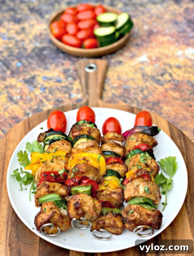 Two finished air fryer chicken and vegetable kebabs presented on a white plate.