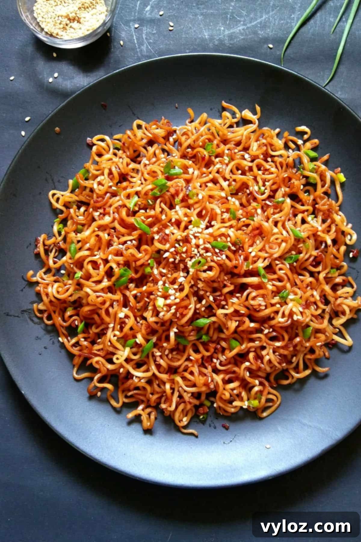 Image showing sesame garlic ramen noodles served on a black plate, garnished with green onions and sesame seeds.