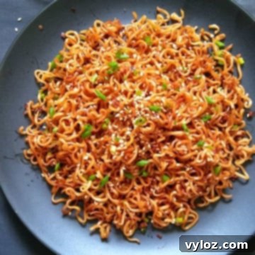Image showing sesame garlic noodles served on a black plate, garnished with green onions and sesame seeds.