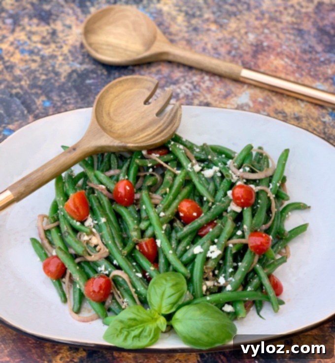 cold green bean salad with tomatoes and feta cheese on a white plate