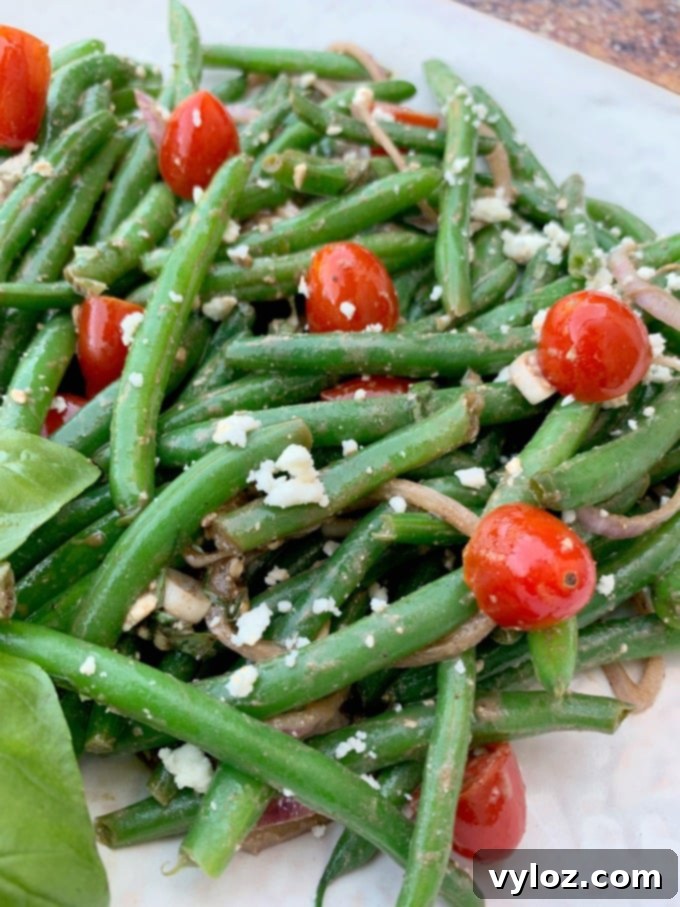 cold green bean salad with tomatoes and feta cheese on a white plate