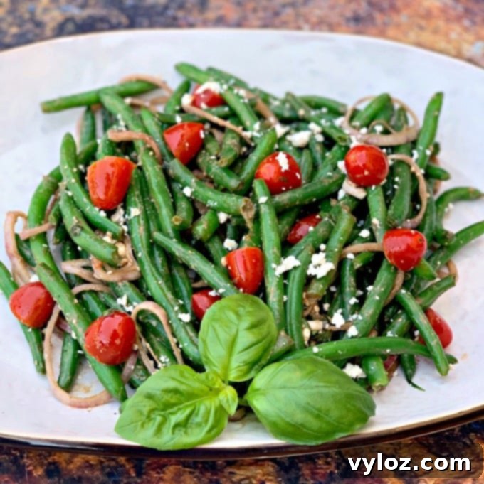 cold green bean salad with tomatoes and feta cheese on a white plate