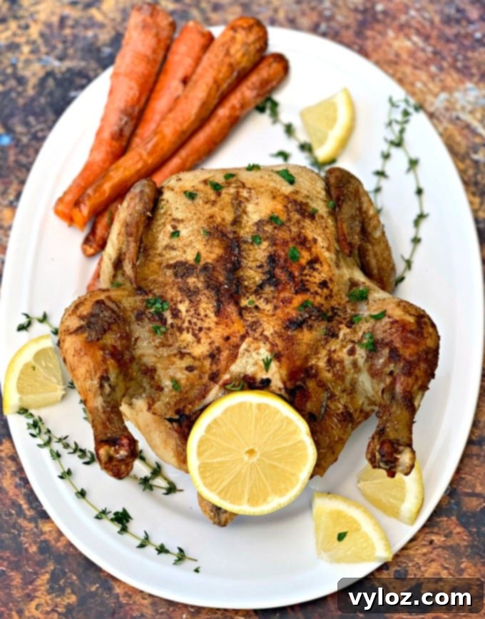 Effortlessly Crispy Air Fryer Whole Chicken 6 air fryer whole chicken on a white plate with fresh lemon and roasted carrots
