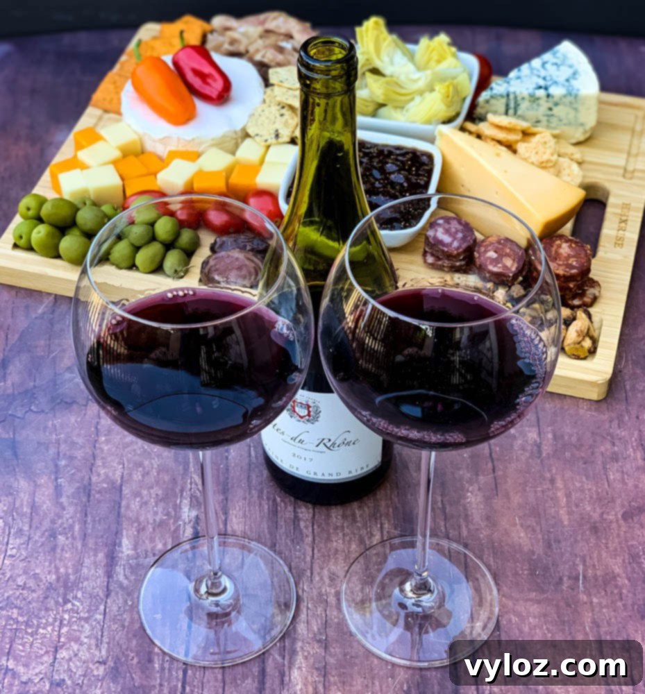 charcuterie board with artichokes, fig spread, cheese, and meat with 2 glasses of red wine