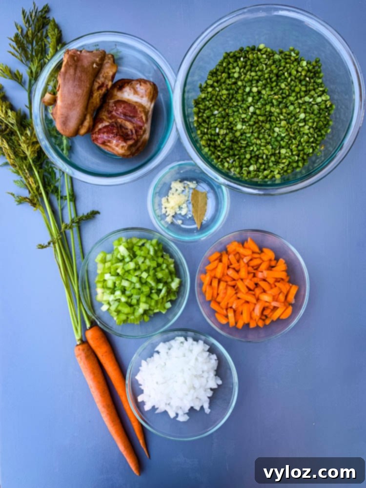 A colorful array of fresh ingredients for split pea soup, including diced carrots, onions, celery, minced garlic, dried green split peas, and savory ham hocks, neatly arranged on a flat surface ready for preparation.