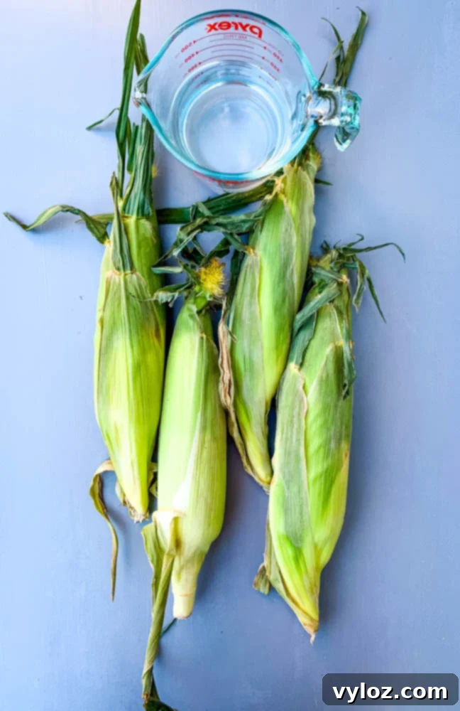 raw unshucked corn and 1 cup of water in a measuring cup, ingredients for Instant Pot corn on the cob.