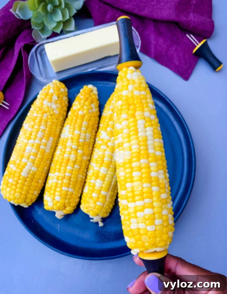 person holding instant pot corn on the cob on a blue plate with a purple napkin, garnished with herbs.