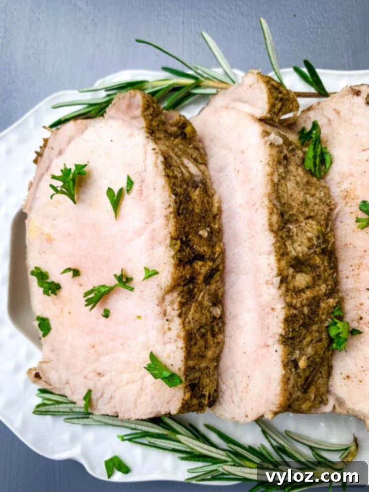 cooked sliced Instant Pot pork loin on a white plate with rosemary