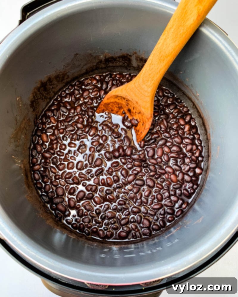 cooked black beans in an instant pot with a wooden spoon