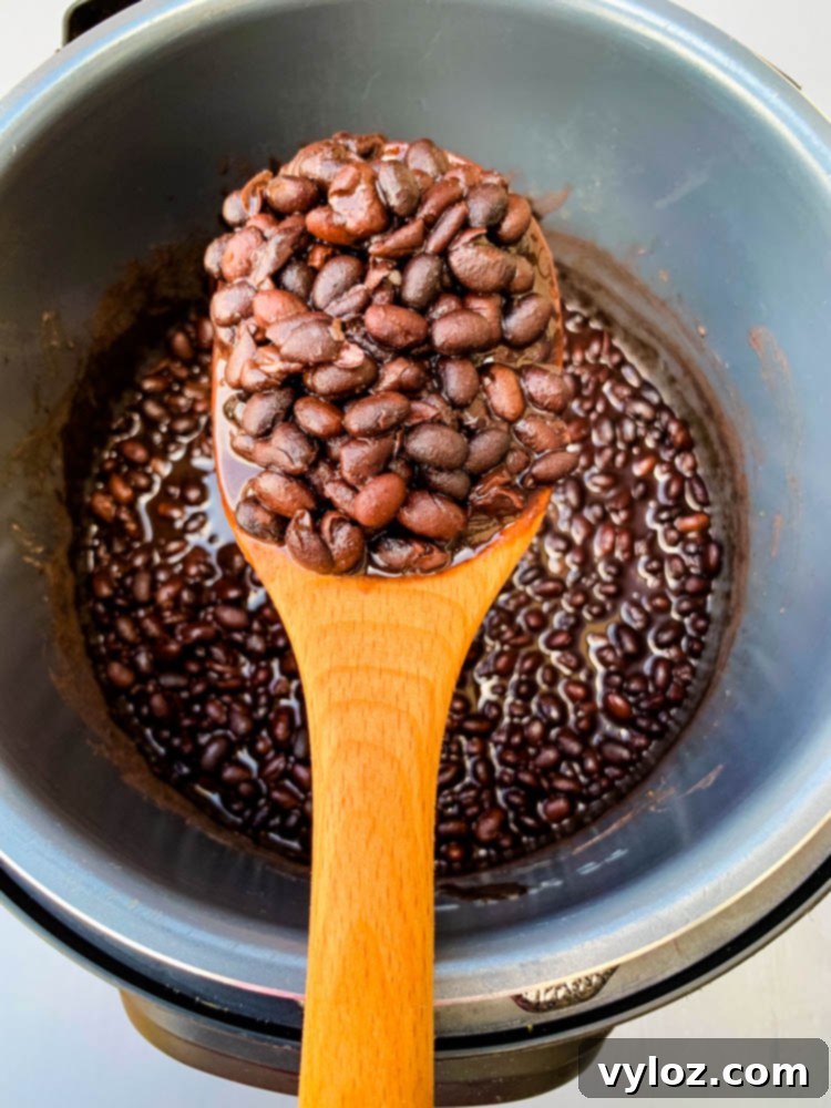 wooden spoon full of cooked black beans in an instant pot