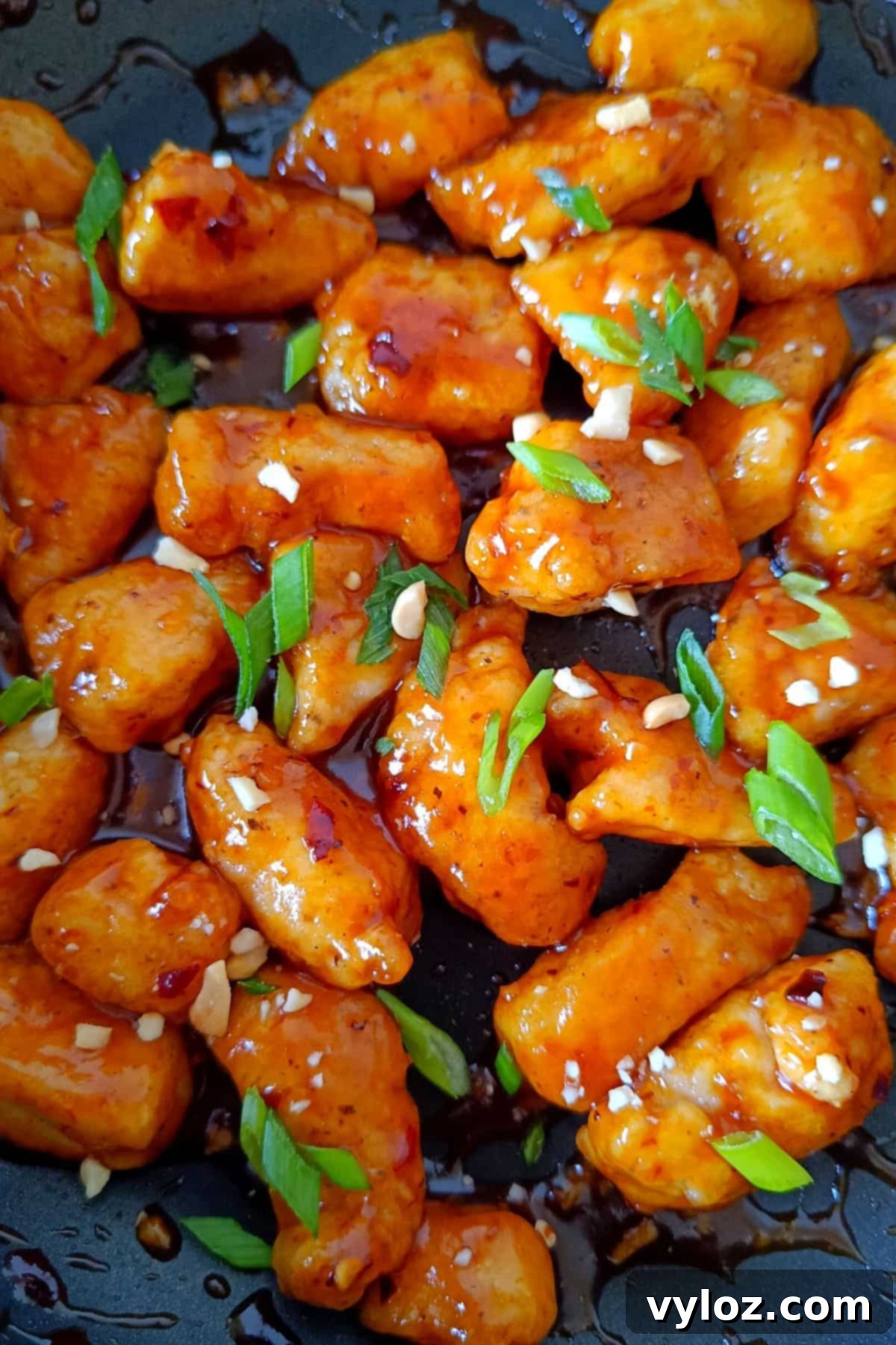 Close-up image showing honey garlic sriracha chicken simmering in a pan, glistening with sauce.