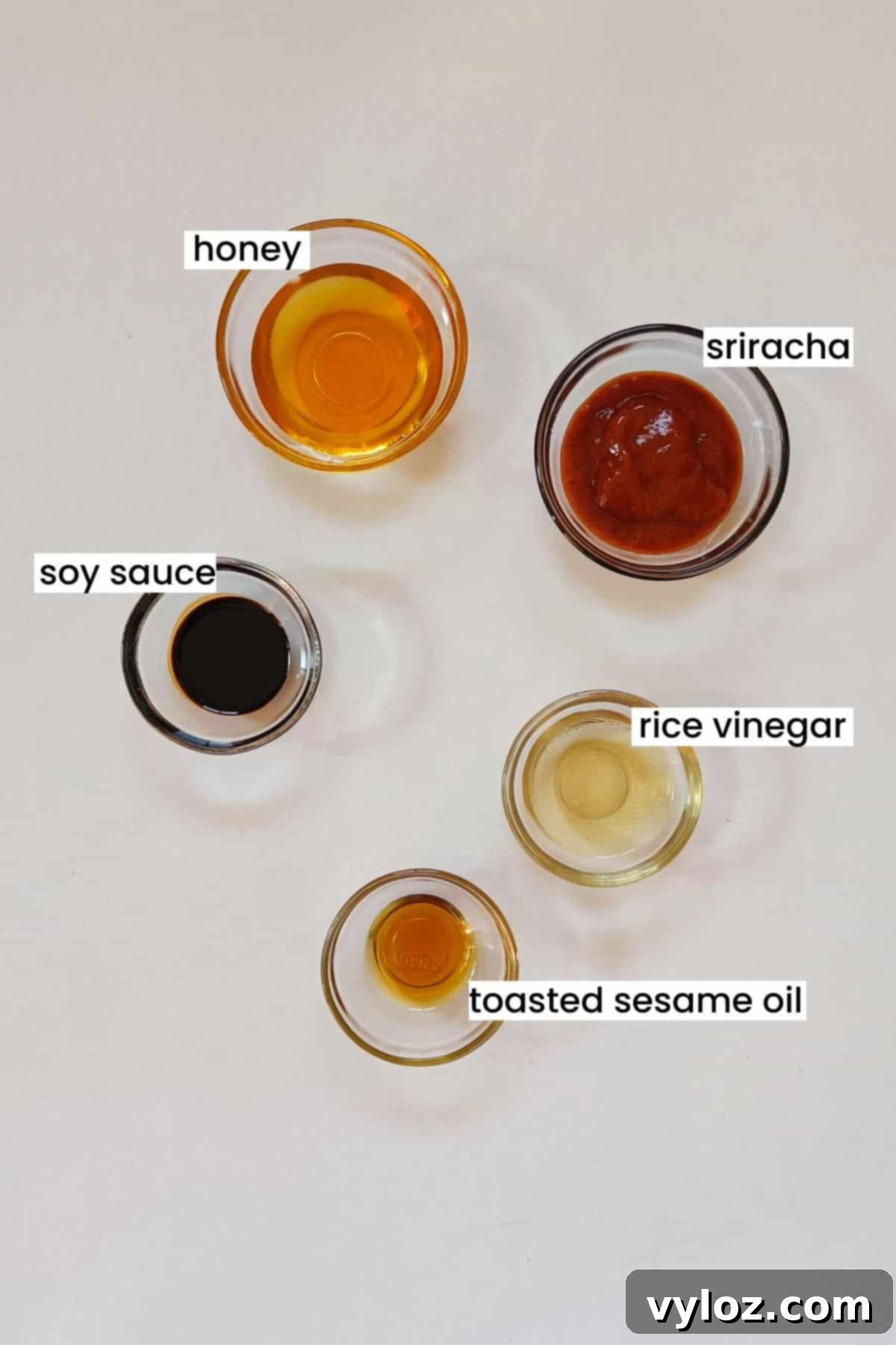 Five key ingredients for the honey sriracha sauce arranged neatly on a white background.