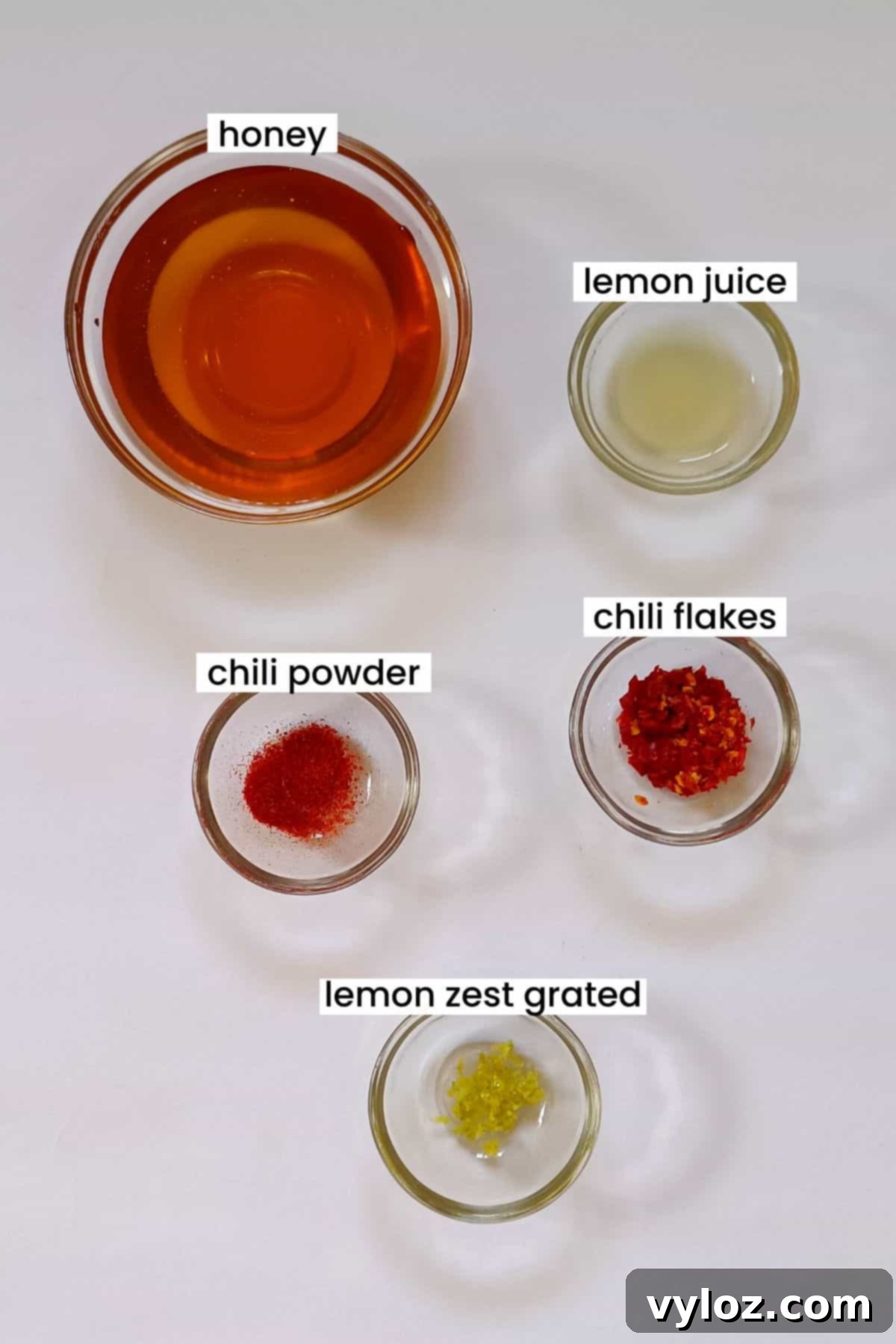 Make Your Own Sweet Heat Honey 3 Image showing hot honey ingredients like honey, chili flakes, and lemons on a white background.