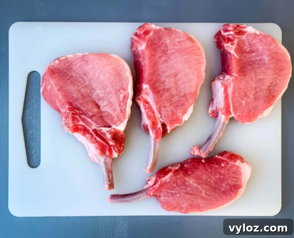 Smothered Keto Pork Chops 3 Raw bone-in pork loin chops on a cutting board, seasoned and ready for cooking