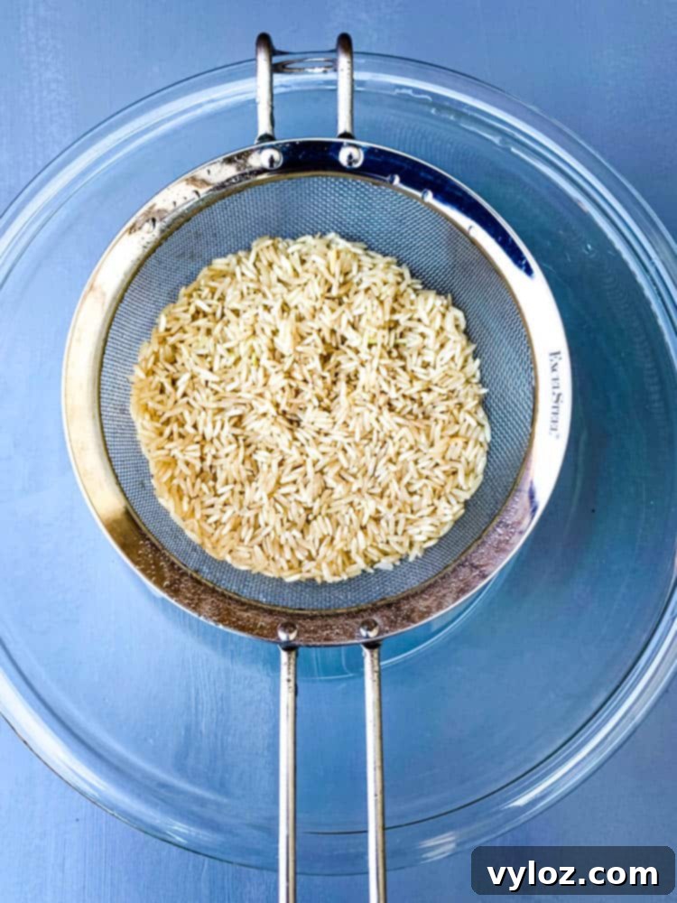 Strained brown rice in a fine-mesh strainer over a glass bowl, showcasing the rinsing process.