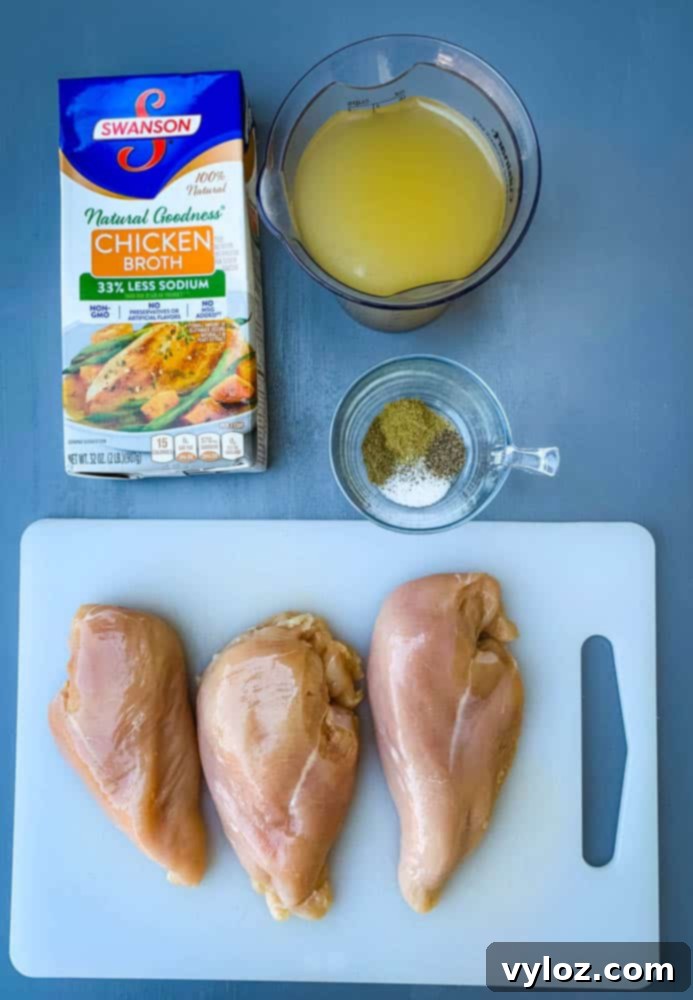 Raw chicken breasts on a cutting board, surrounded by chicken broth, various spices, and fresh herbs.