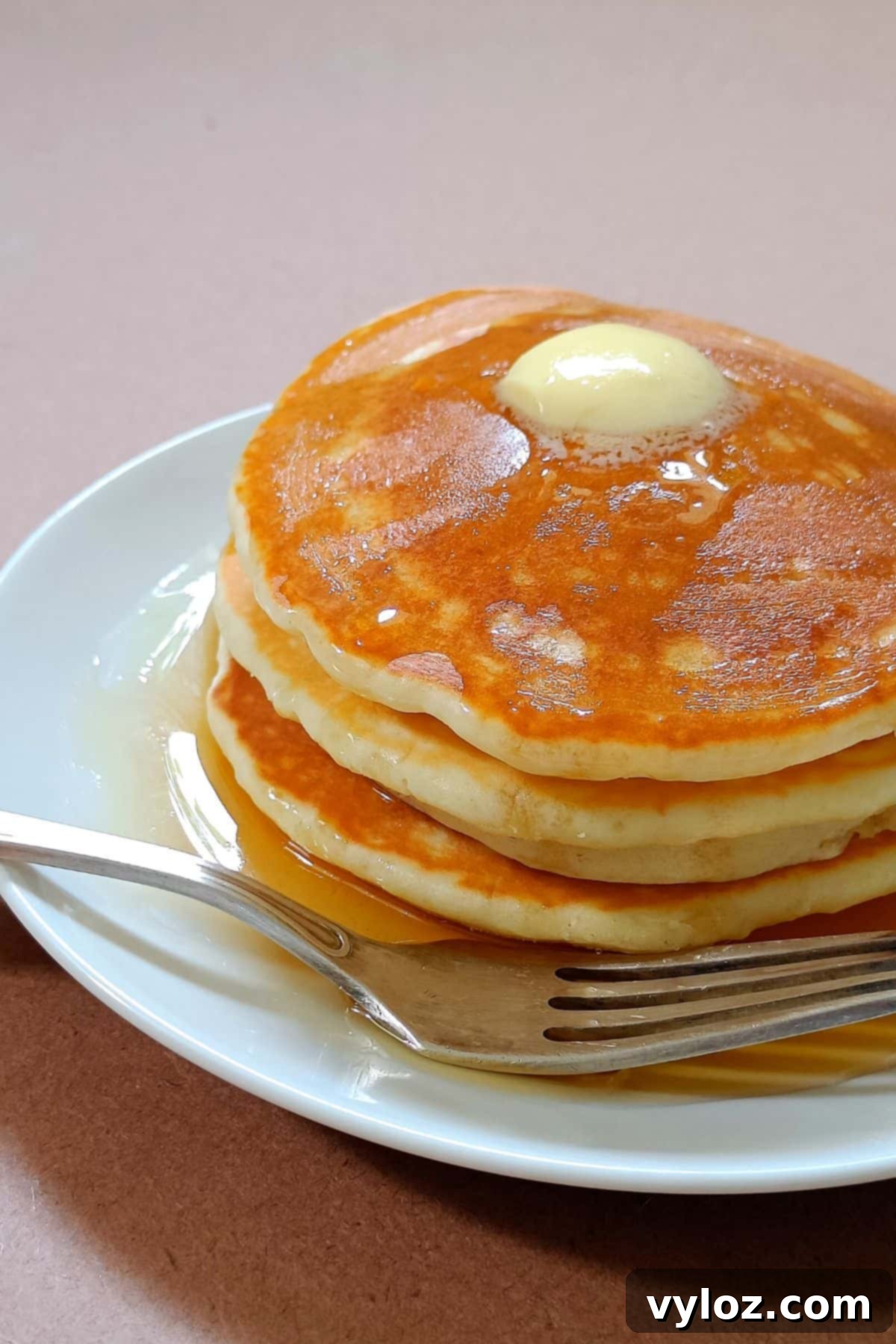 Image showing a stack of golden, fluffy pancakes served on a white plate, ready to be enjoyed.