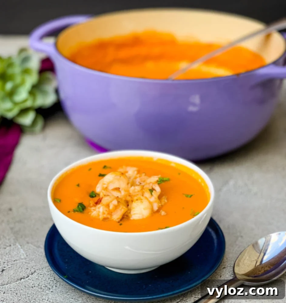 A beautifully composed flat lay of creamy homemade lobster bisque served in a white bowl with a stylish purple napkin, accompanied by the purple Dutch oven it was cooked in, highlighting a complete, luxurious meal.