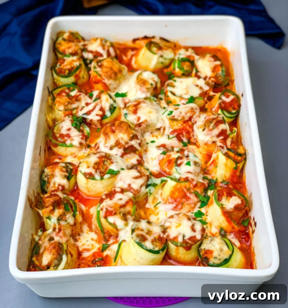 Quick Zucchini Lasagna Pinwheels 2 Delicious zucchini lasagna roll ups in a white baking pan, topped with shredded melted cheese and herbs, ready to serve.
