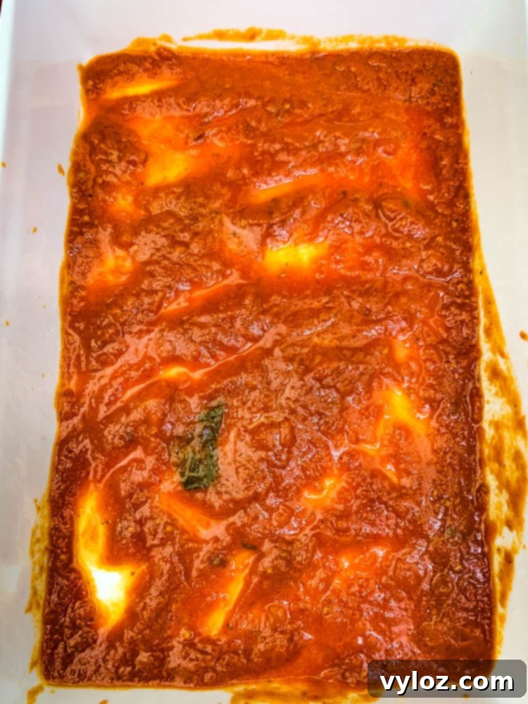 Quick Zucchini Lasagna Pinwheels 7 Marinara sauce spread evenly at the bottom of a white ceramic baking dish, ready for zucchini lasagna roll ups.