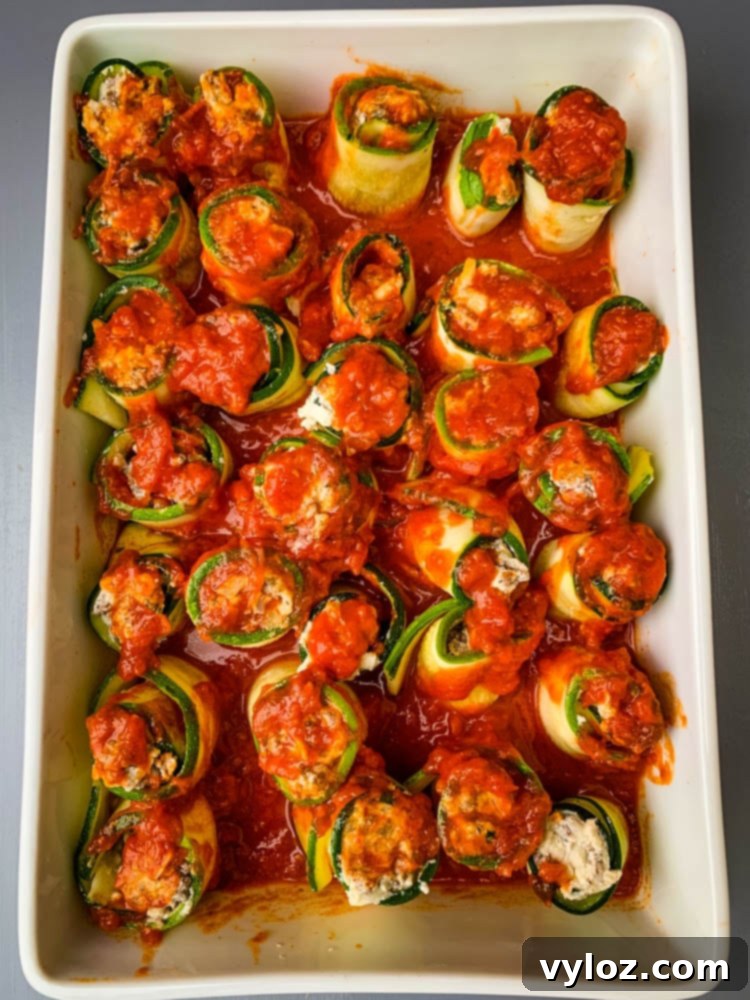 Quick Zucchini Lasagna Pinwheels 9 Zucchini lasagna rolls covered in marinara sauce, ready for mozzarella cheese and baking in a white dish.