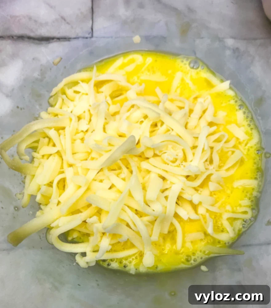 Shredded mozzarella cheese and eggs being mixed in a bowl, forming the base for delicious chaffles.