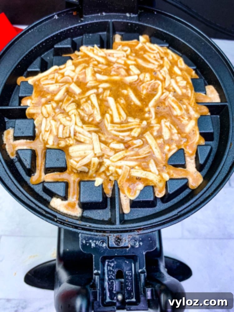 Cinnamon roll chaffle batter poured into a preheated waffle iron, ready to cook.