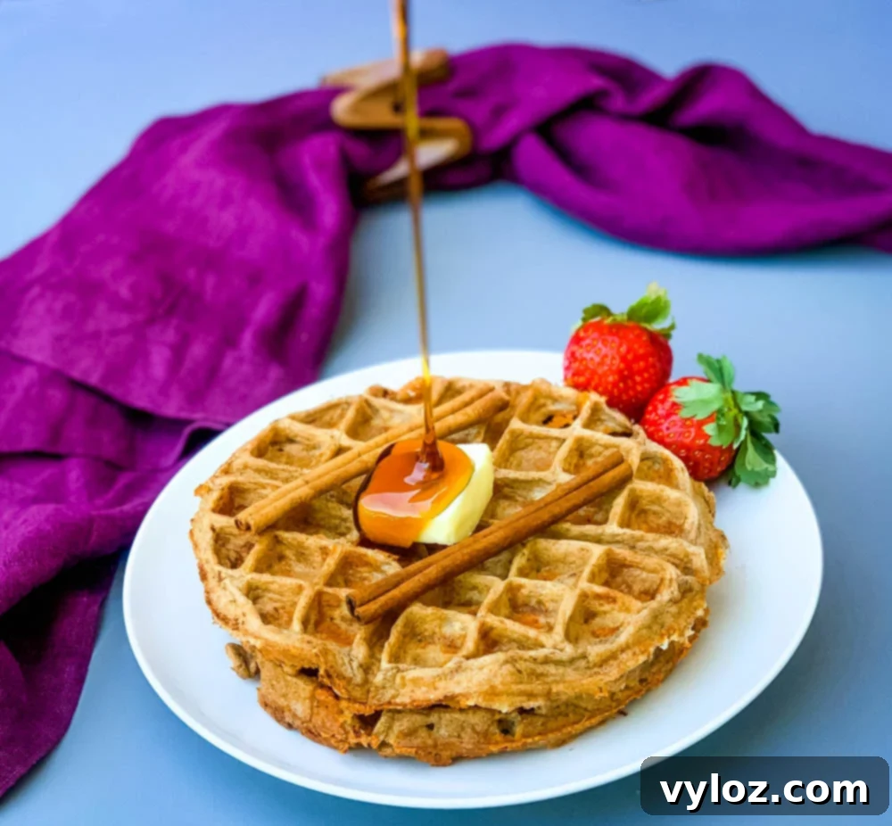 Two keto low carb cinnamon roll chaffles on a white plate, topped with a generous pat of butter and a drizzle of sugar-free syrup.
