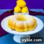air fryer lemon cake on a white cake stand with fresh lemons