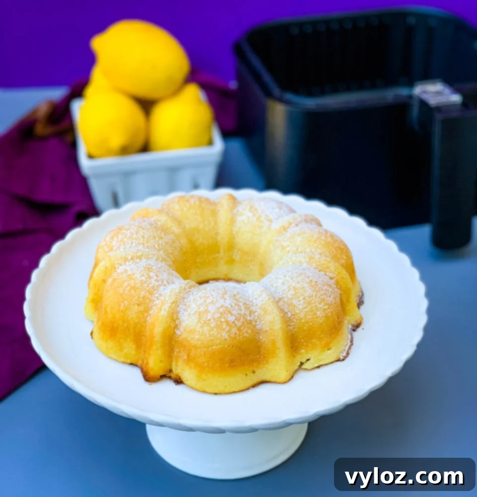 air fryer lemon cake on a white cake stand with fresh lemons
