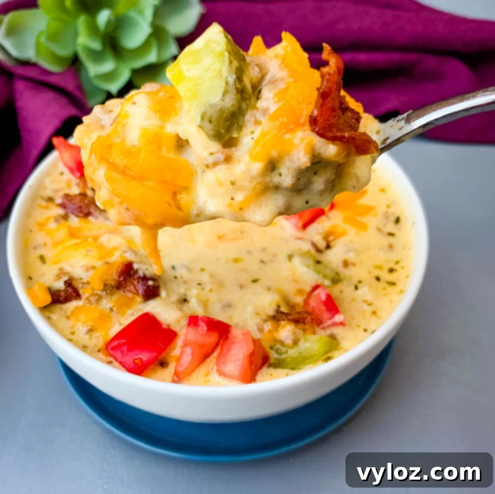 Savory Keto Cheeseburger Bliss 11 A close-up of a spoonful of keto cheeseburger soup, beautifully garnished with pieces of bacon, pickles, and tomatoes.