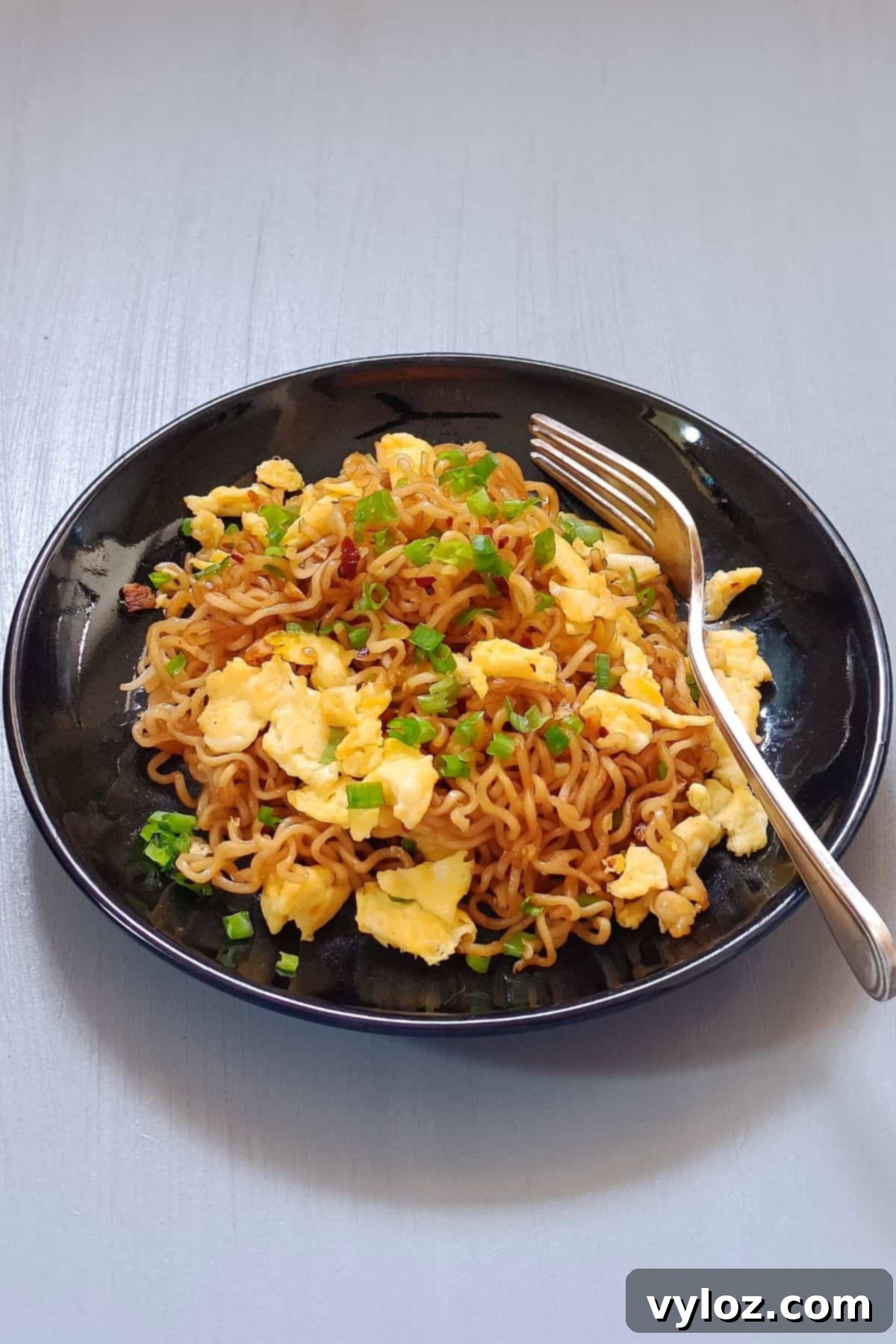 A vibrant bowl of ramen scrambled eggs, artfully garnished with fresh green onions, ready to be enjoyed.
