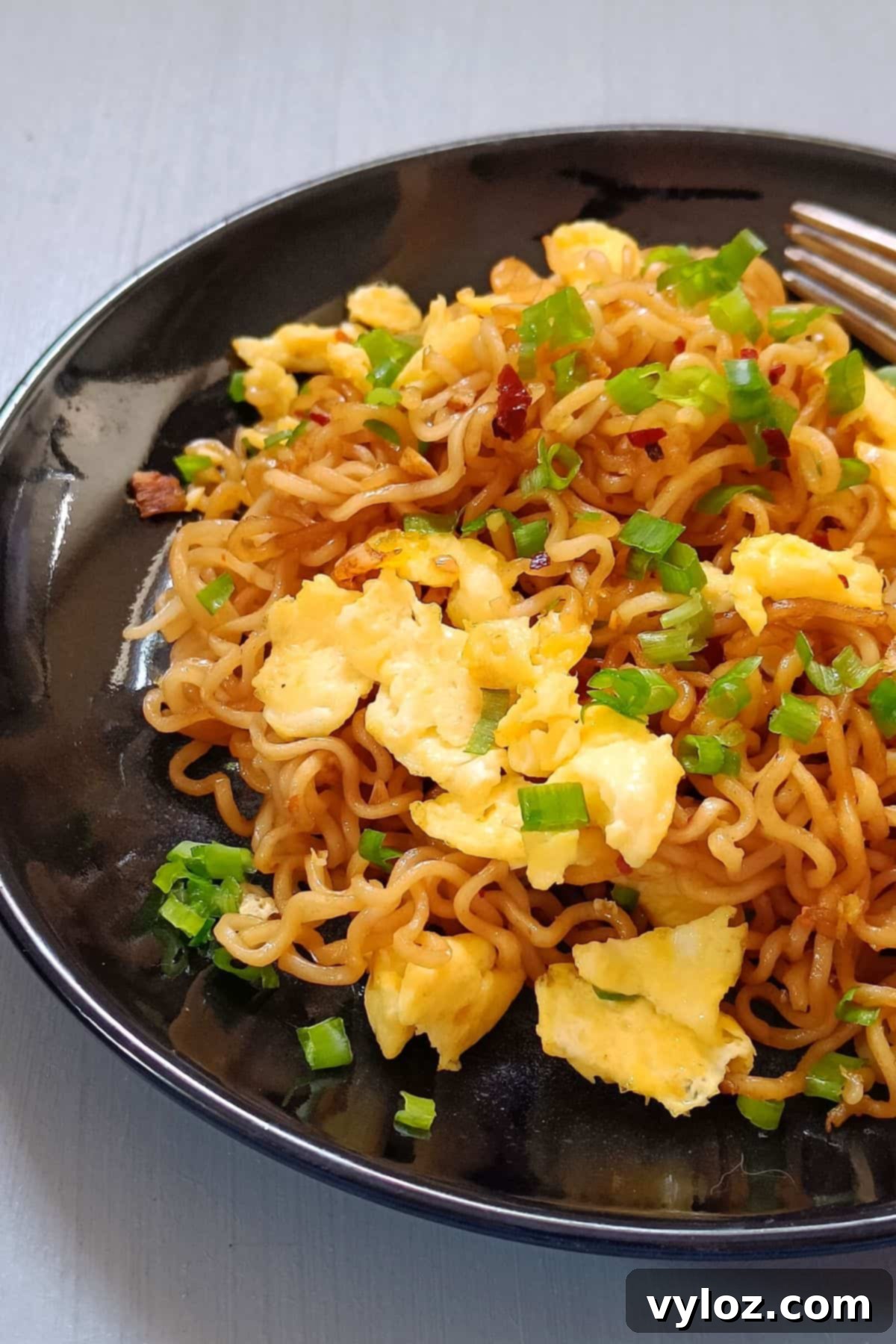 A close-up shot of ramen with scrambled eggs, garnished with fresh green onions, served in a rustic bowl, highlighting its vibrant colors and inviting texture.