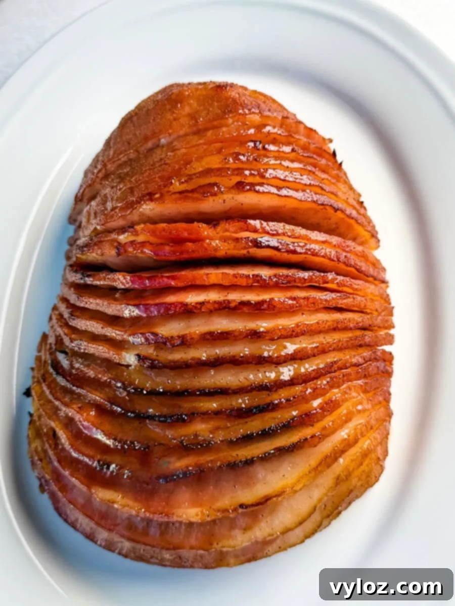 A perfectly cooked, spiral-sliced honey-glazed ham is presented on a white serving platter, exhibiting its appealing caramelized, shiny finish and tender, juicy slices.