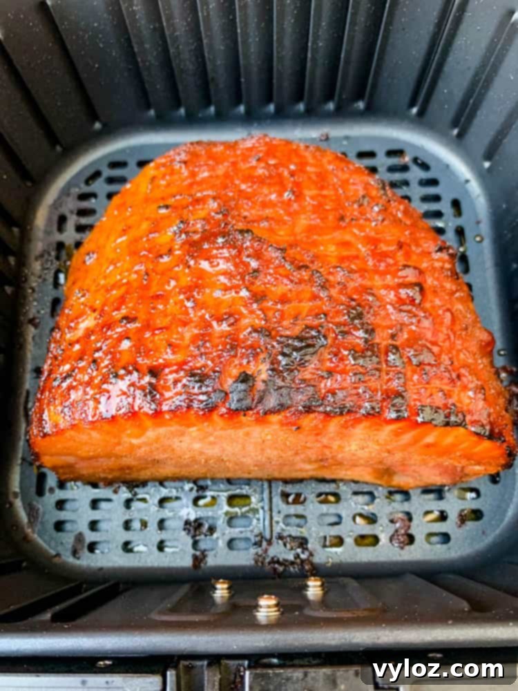 A boneless ham, generously coated in glaze, is positioned inside an air fryer, ready for the cooking process that will yield a juicy and flavorful holiday centerpiece.