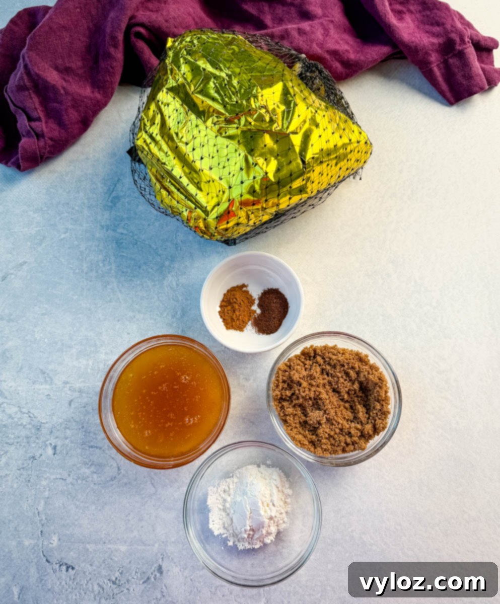Ingredients for air fryer honey glazed ham, including bowls of brown sugar, honey, cornstarch, and a small dish of ground cinnamon and cloves, arranged next to a packaged ham wrapped in gold foil and netting on a clean countertop.