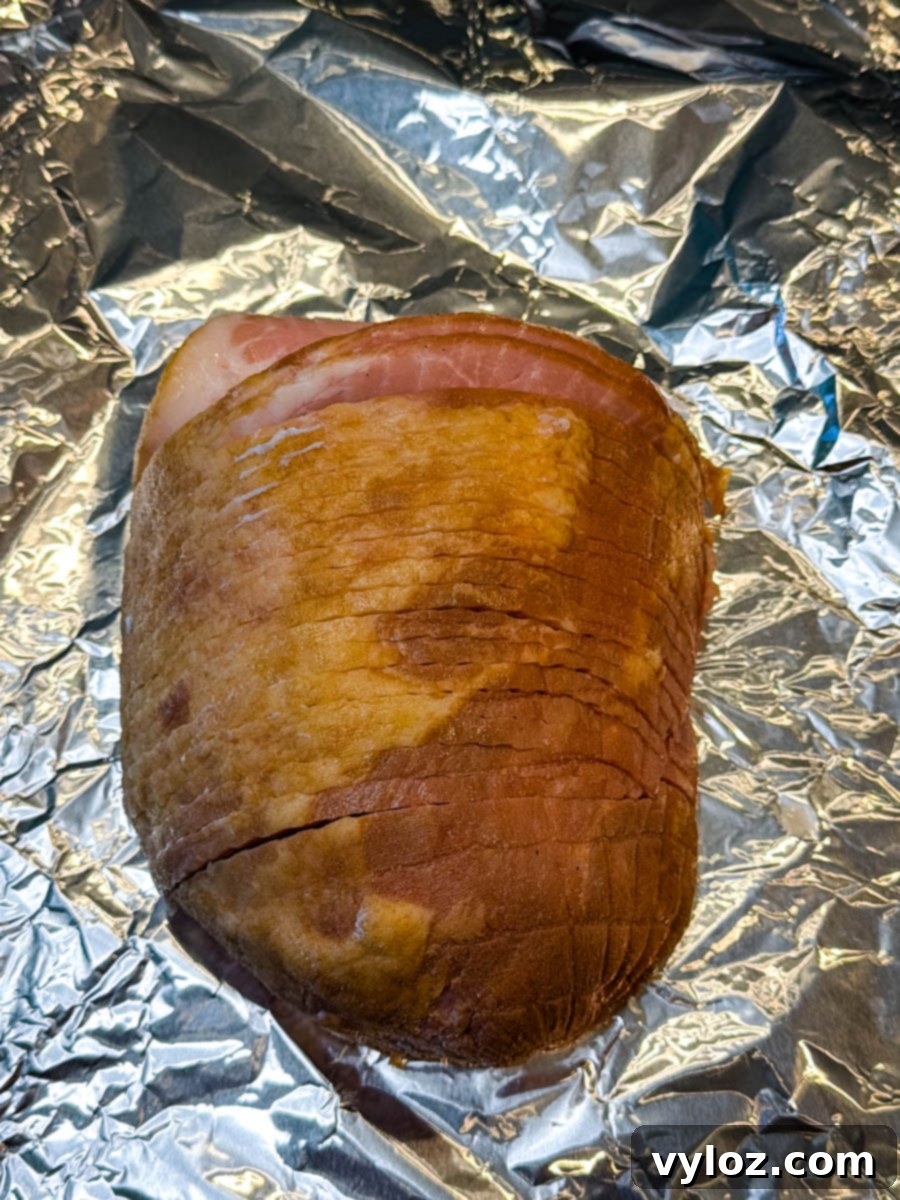 A small, pre-cooked boneless ham resting on a sheet of aluminum foil, perfectly positioned and ready for seasoning and glazing before being placed into the air fryer.
