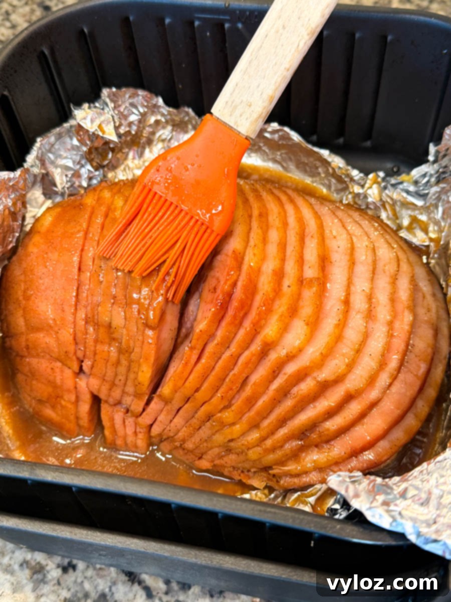 A close-up view of a honey-glazed ham resting in an air fryer basket, with the rich, bubbling glaze coating its surface, just before the final caramelization stage.