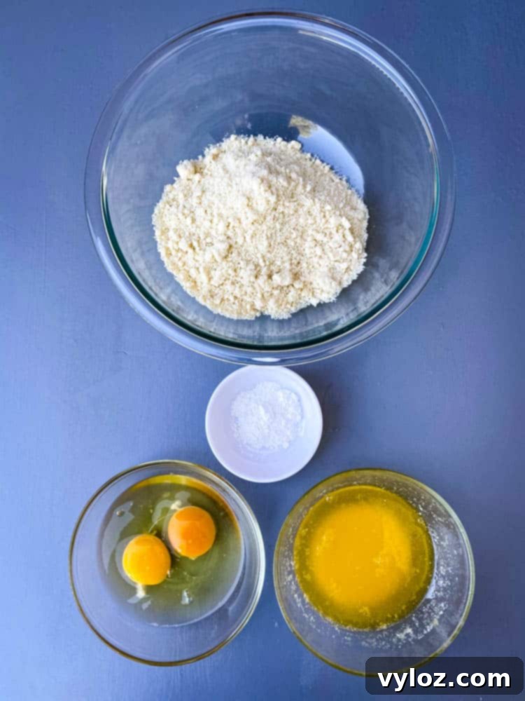 Key ingredients for making light and fluffy keto low carb biscuits, including almond flour, eggs, melted butter, and baking powder, laid out on a kitchen surface.