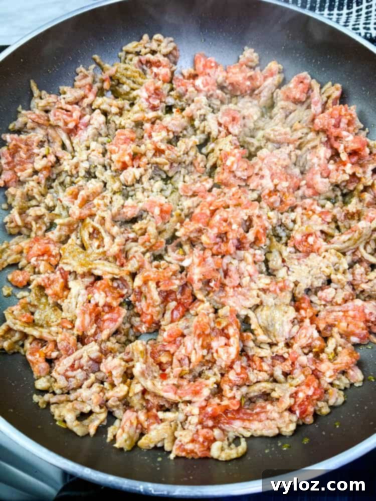 Ground sausage actively cooking in a skillet, breaking down into crumbles for the rich keto low carb gravy.