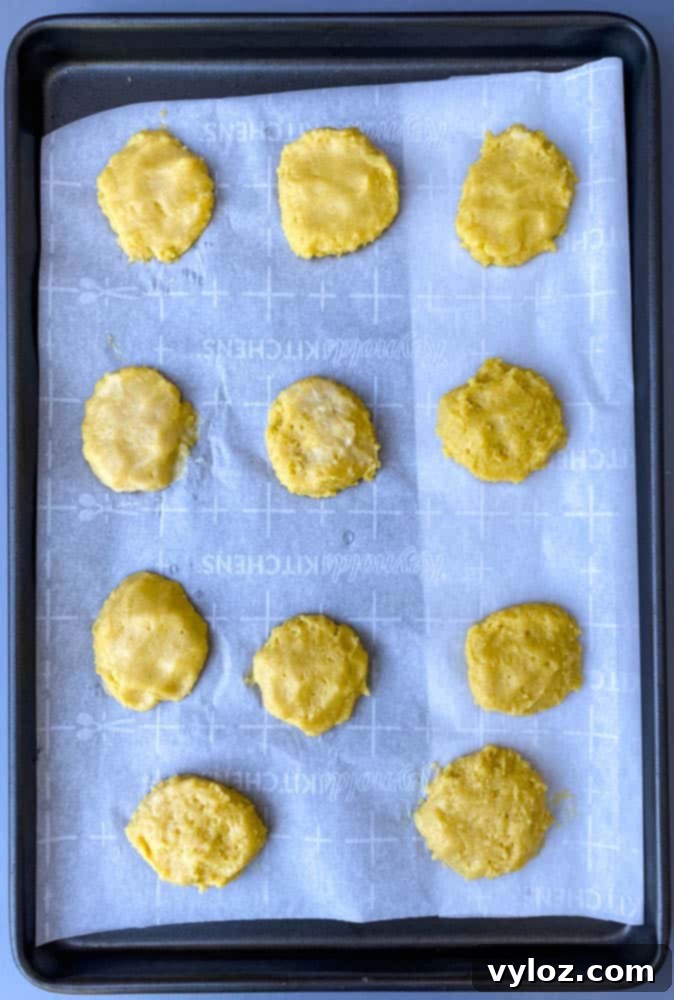 Rows of perfectly scooped keto low carb biscuit dough, flattened and arranged on parchment paper on a baking sheet, ready for the oven.