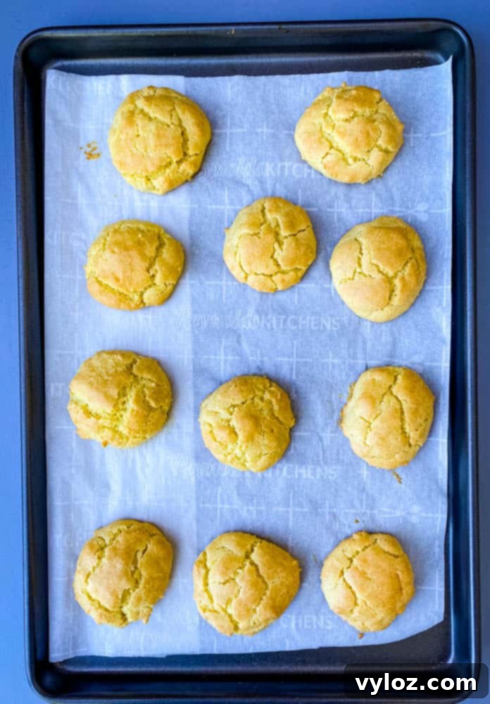 A batch of golden-brown keto low carb biscuits, fresh from the oven, cooling on parchment paper on a baking sheet.