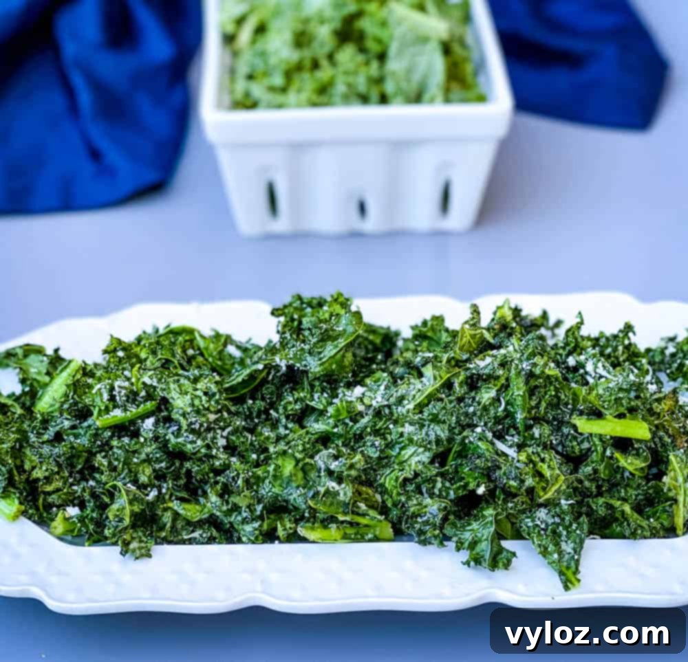Crispy air fryer kale chips on a white plate with freshly grated Parmesan cheese