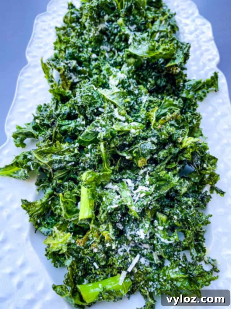 Close-up of crispy air fryer kale chips on a white plate, seasoned with Parmesan cheese