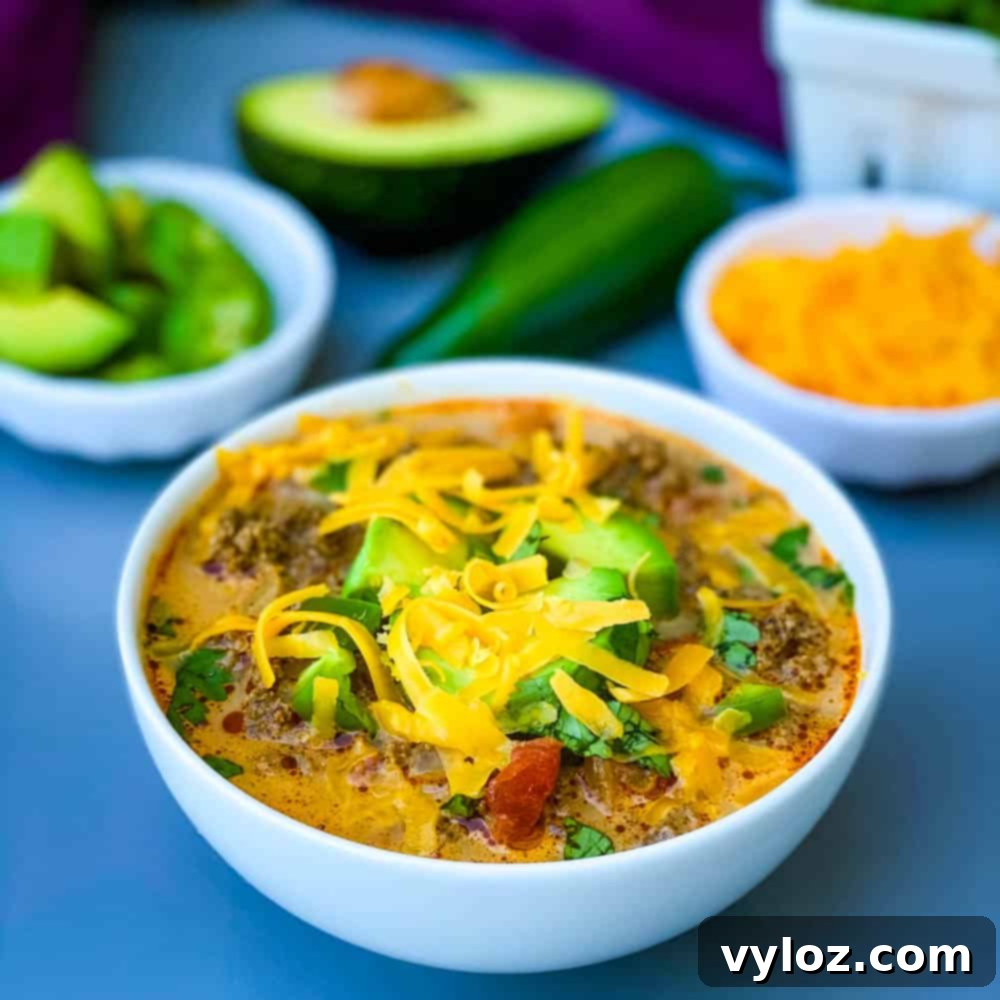 Keto low-carb taco soup with shredded cheese, avocado, and jalapenos in a white bowl, garnished beautifully for serving.